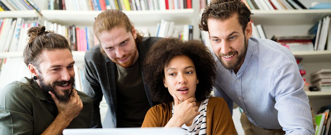 Three colleagues looking at a laptop screen together in an office