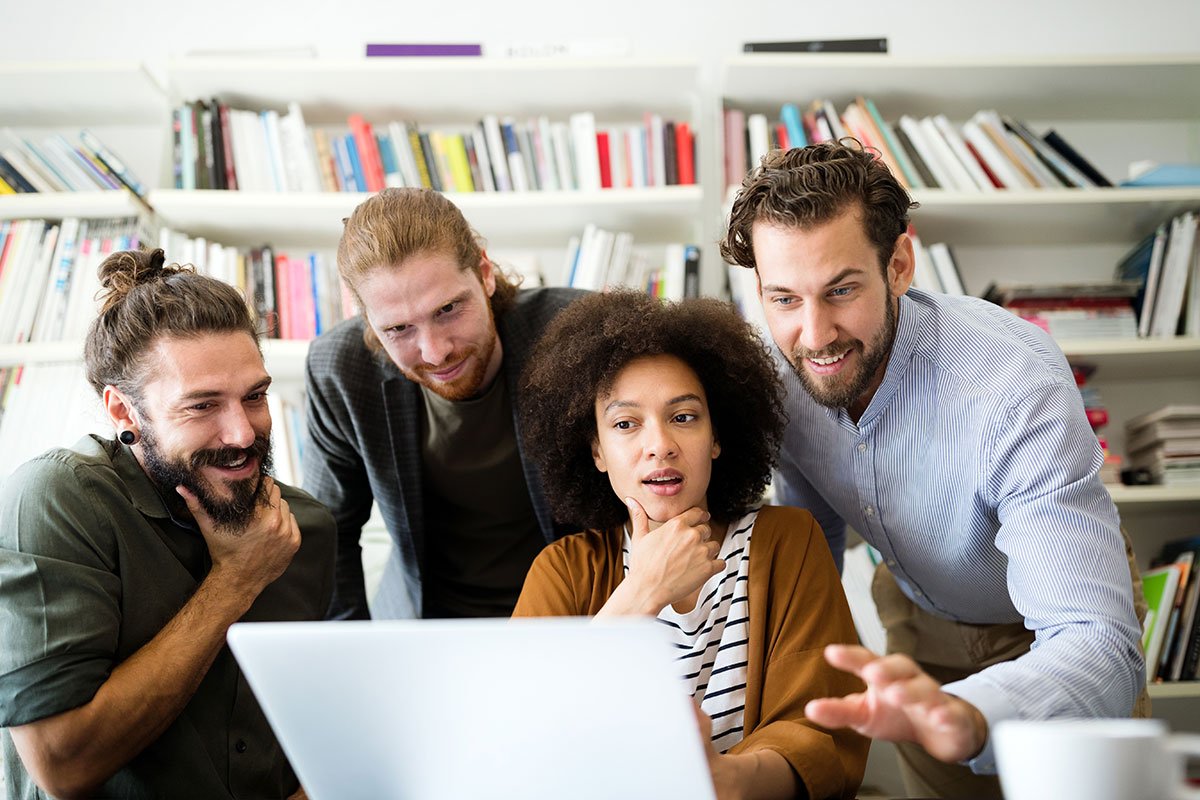 Three colleagues looking at a laptop screen together in an office