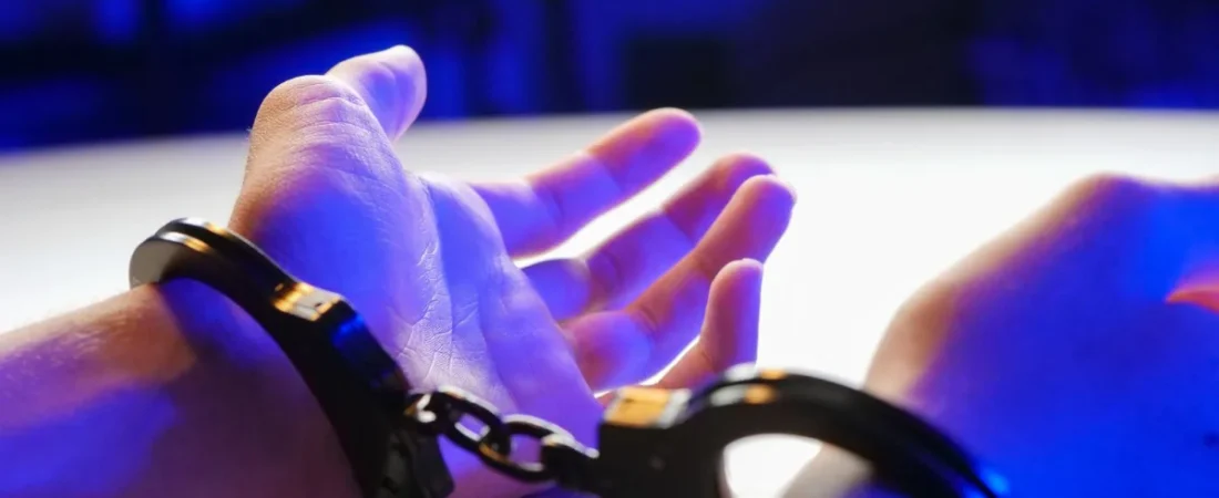 Handcuffed hands under blue police lights
